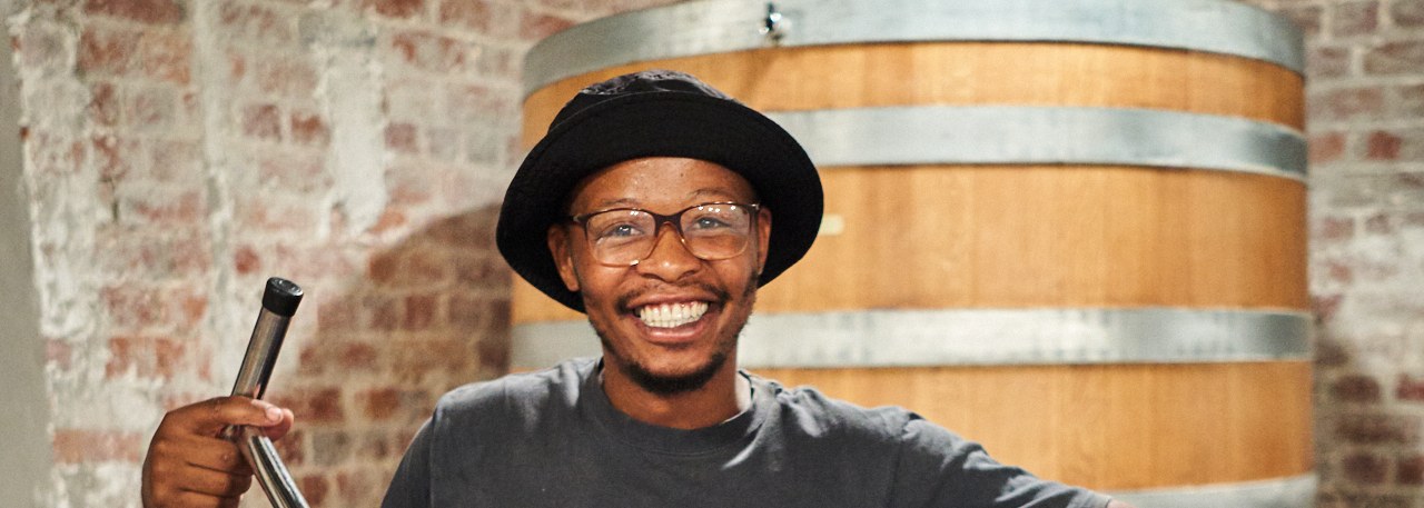 Banele Vakele smiling in front of a wooden wine vat